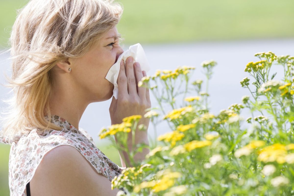 woman blowing nose into tissue in front of flowers